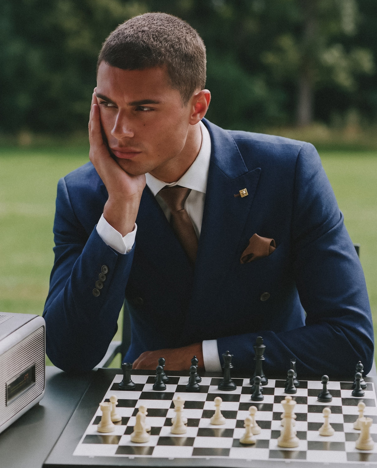 Man in a navy double breasted suit considering his next move at a chessboard
