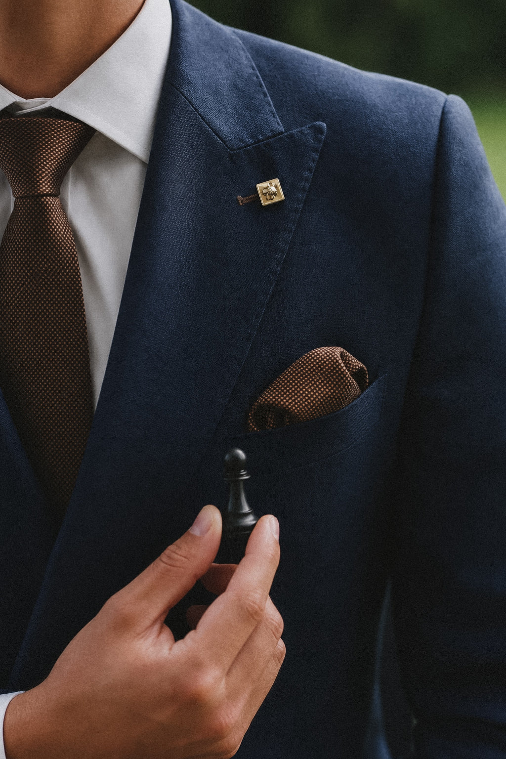 Lapel pin, brown tie and pocket square detail on a navy suit